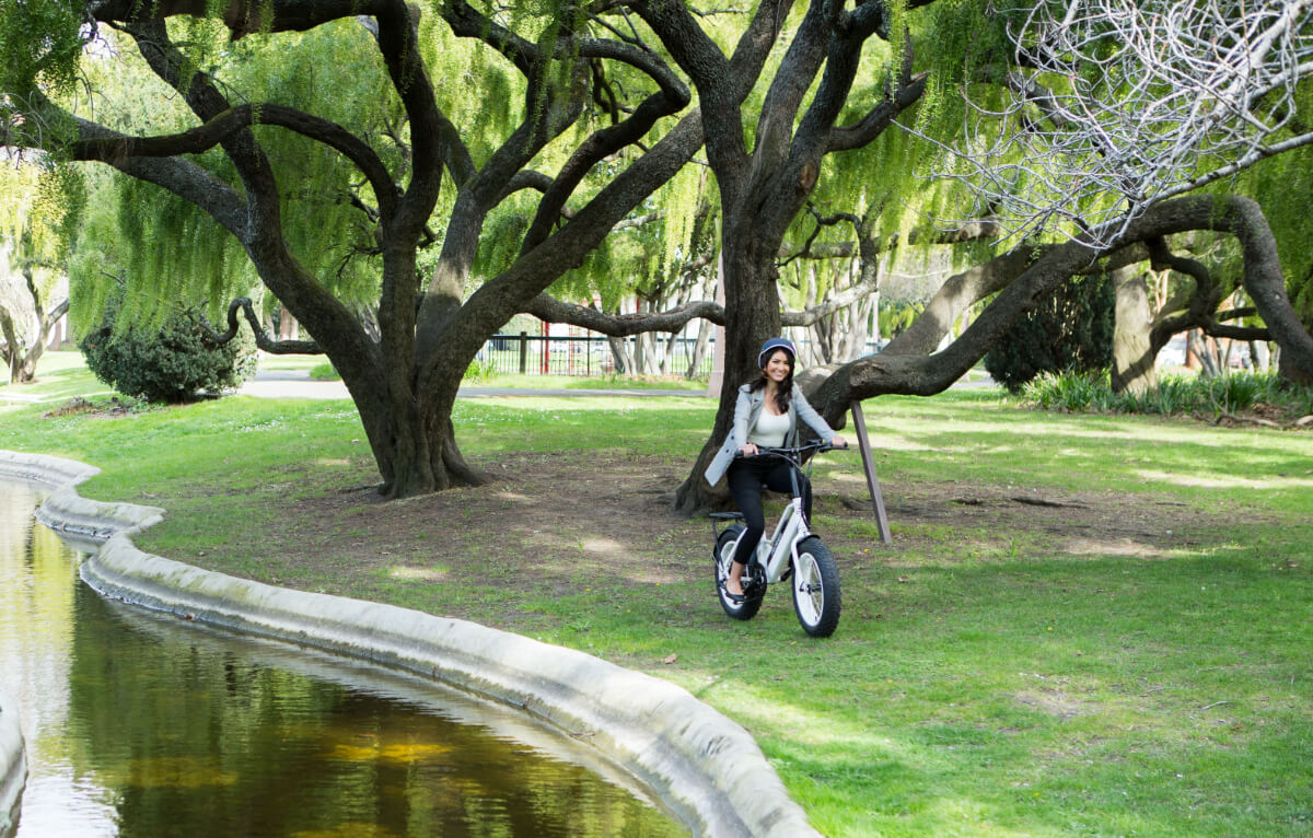 A woman smiling and riding her e-bike in the park.