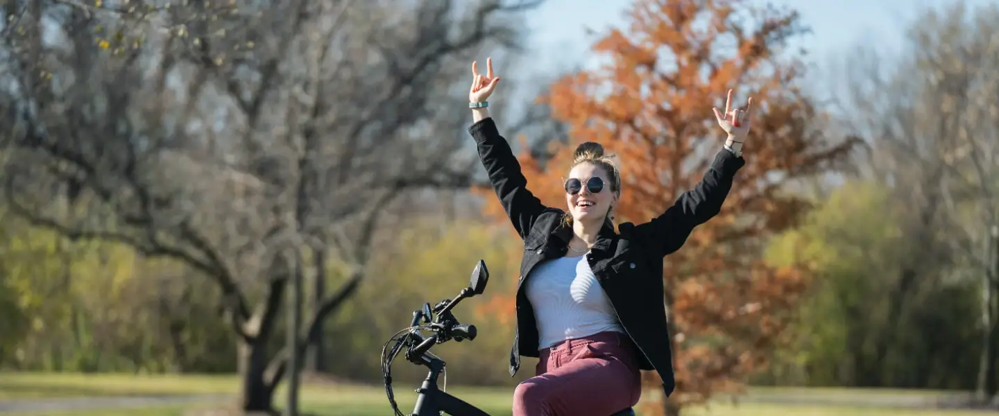 A young smiling woman on an e-bike in front of trees in fall in a park