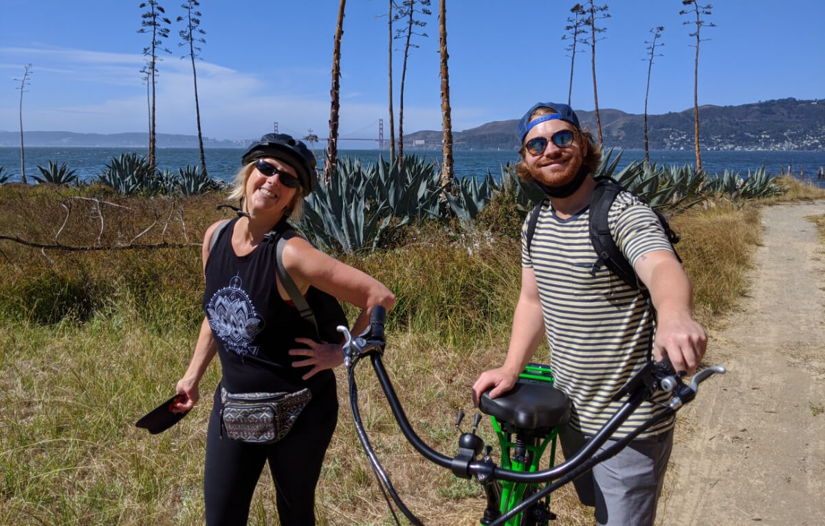 Two happy people smiling with their e-bikes by the ocean