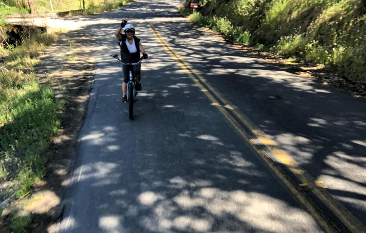 A woman riding her e-bike and smiling on a road in the shade