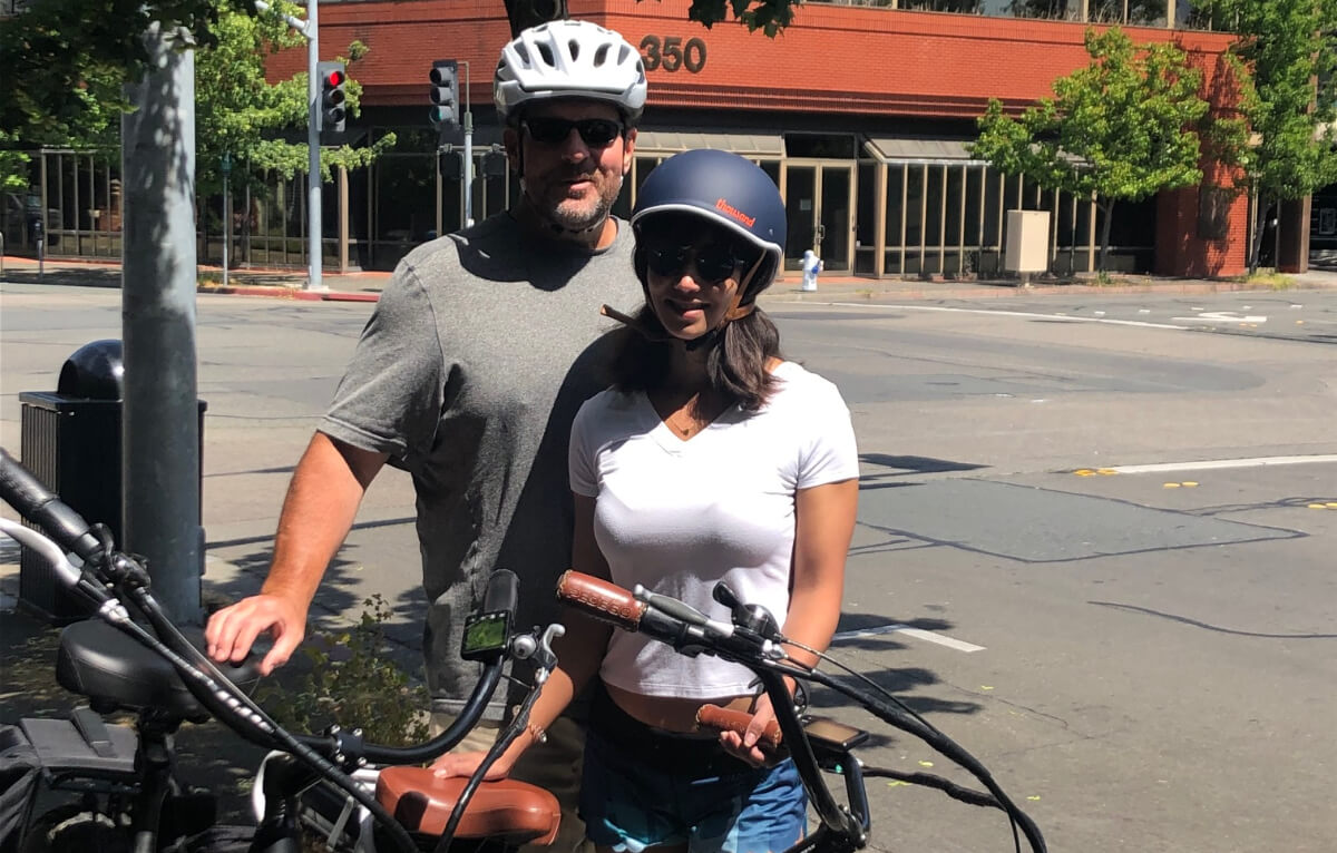 Two people smiling by their e-bikes with helmets on